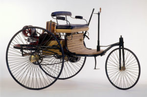 Auf dem Foto sieht man das erste Auto von Carl Benz. Es ähnelt eher einem überdimensioniertem Dreirad, besitzt kein Dach und ist größtenteils aus Holz gebaut.